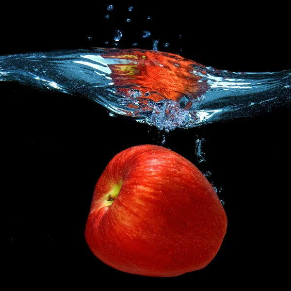 Roter Apfel fiel ins Wasser mit Spritzer isoliert auf schwarz — Stockfoto