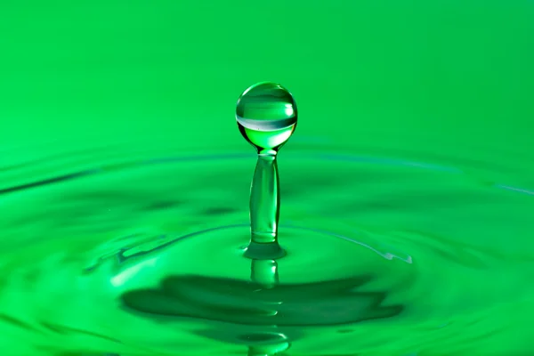 Green droplet splashing in clean water — Stock Photo, Image