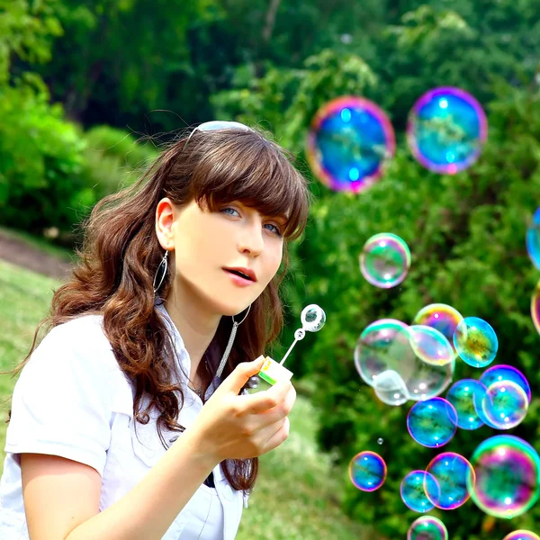Молодая девушка надувает мыльные пузыри весной зеленого цвета — стоковое фото