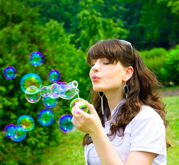 Молодая девушка надувает мыльные пузыри весной зеленого цвета — стоковое фото