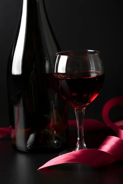Glass of red wine and red ribbon over black back — Stock Photo, Image