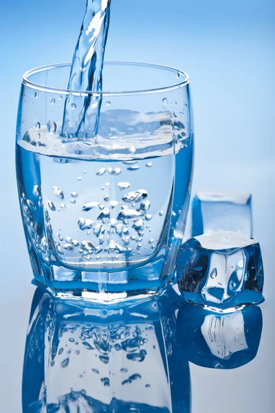 Water splashing into glass with ice cubes — Stock Photo, Image