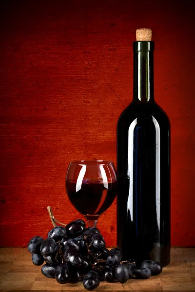 Garrafa de vinho, vidro e uvas sobre tinto — Fotografia de Stock
