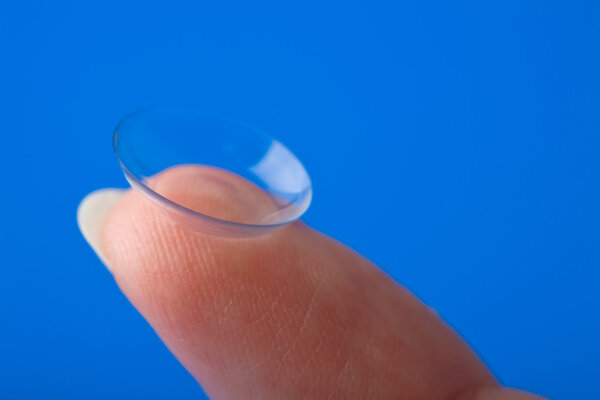 Finger holding contact lens over blue background