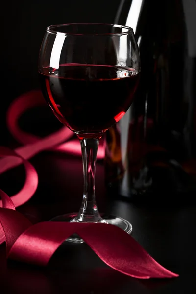 Glas rode wijn en rood lint op zwarte achtergrond — Stockfoto