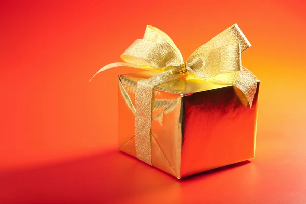Caja de regalo de oro con lazo sobre fondo rojo — Foto de Stock