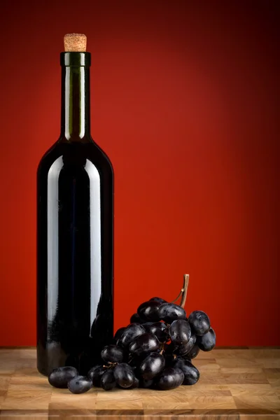 Bottle of wine and grapes over red background — Stock Photo, Image