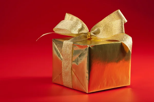 Caixa de presente dourada sobre fundo vermelho — Fotografia de Stock