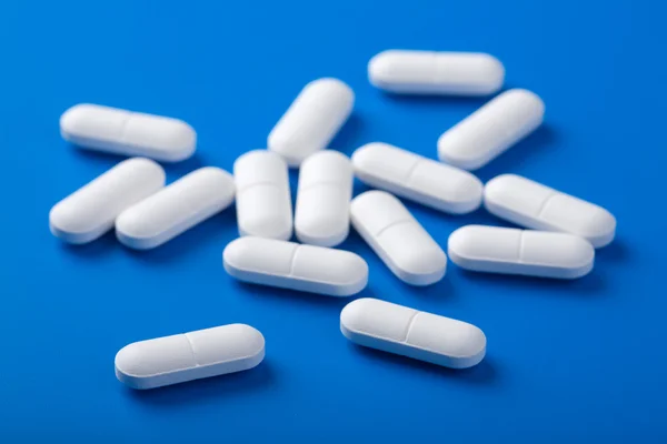 Pílulas brancas sobre azul — Fotografia de Stock