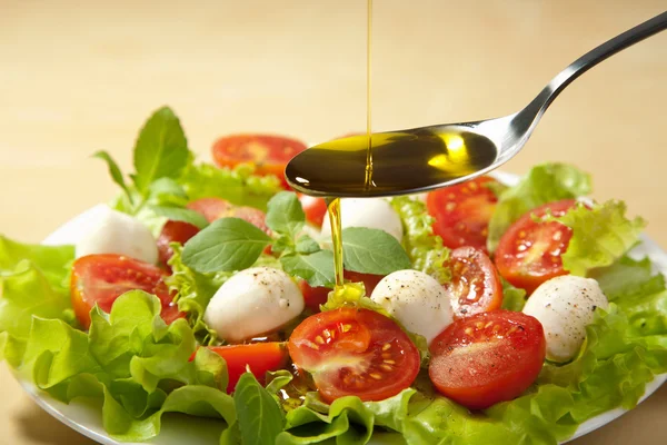 Olive oil pouring over salad — Stock Photo, Image