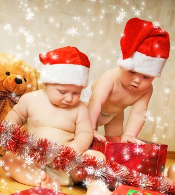 Two adorable toddlers in Christmas hats packing presents clipart