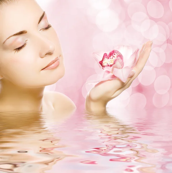 Mooie jonge vrouw met orchid weerspiegeld in water — Stockfoto