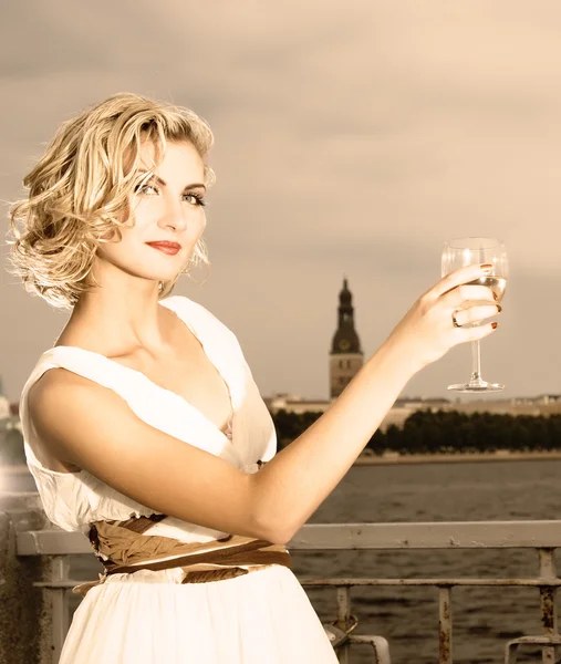 Krásná blonďatá dívka pije šampaňské nedaleko řeky při západu slunce t — Stock fotografie