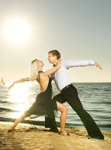 Hermosa pareja joven bailando tango en la playa al atardecer — Foto de Stock