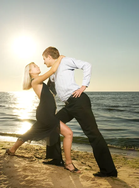 Mooie jonge paar tango dansen op het strand bij zonsondergang — Stockfoto