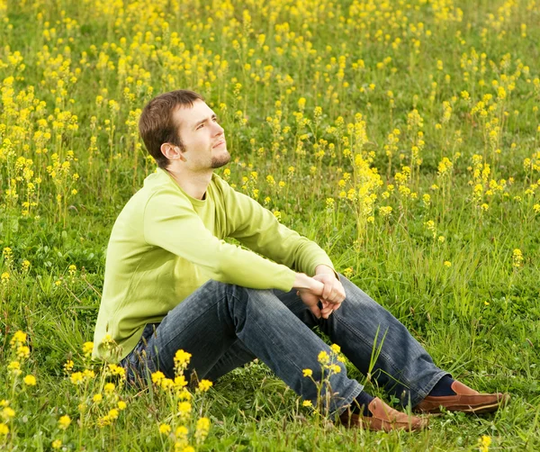 Ontspannen jonge man zit in een bloem veld — Stockfoto