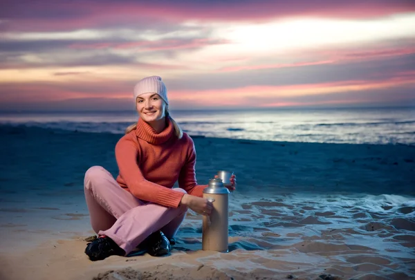在日落时在沙滩上喝着热茶的美丽女人 — 图库照片