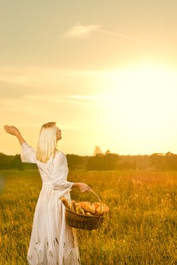 Woman with a basket full of fresh baked bread at sunset clipart