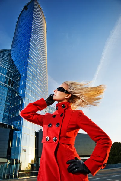 Beautiful young blond talks on the phone. Modern building behind — Stock Photo, Image