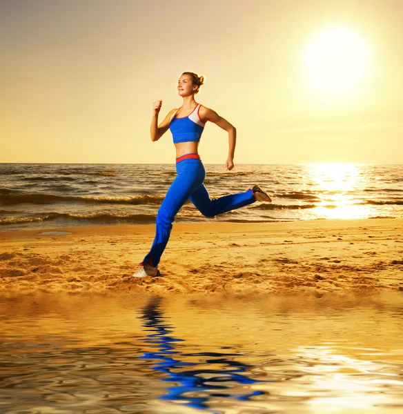 Красива молода жінка біжить на пляжі на заході сонця — стокове фото