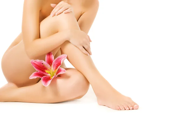 ขาผู้หญิงที่มีดอกลิลลี่สีชมพูแยกกันบนพื้นหลังสีขาว ภาพสต็อก