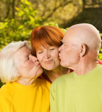 Senior parents kissing their daughter outdoors clipart