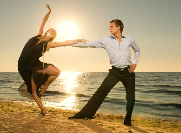Mooie jonge paar tango dansen op het strand bij zonsondergang — Stockfoto