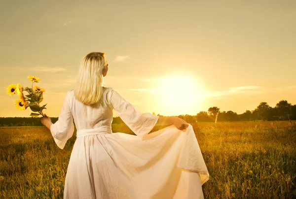 Vacker kvinna med solrosor i fältet vid solnedgången — Stockfoto