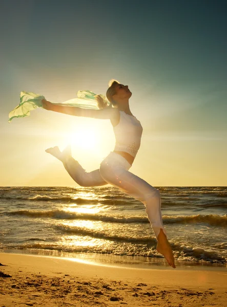 Красива молода жінка стрибає на пляжі на заході сонця — стокове фото