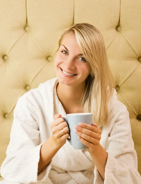 Mooie jonge vrouw zittend op een bed en drinken cofee in de — Stockfoto