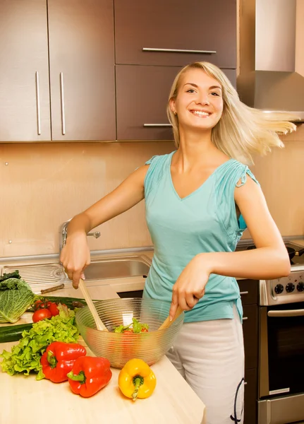 Beautiful young woman mixing vegetable salad in a glass bowl — Stock Photo, Image