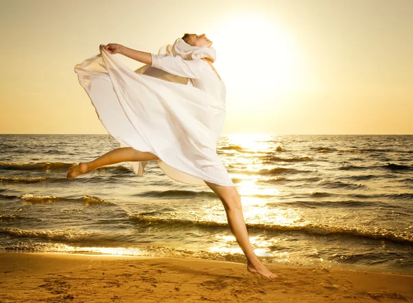 Schöne junge Frau springt bei Sonnenuntergang an einen Strand — Stockfoto