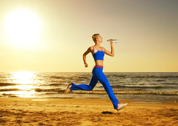 Mulher bonita correndo em uma praia ao pôr do sol (tiro real, b — Fotografia de Stock