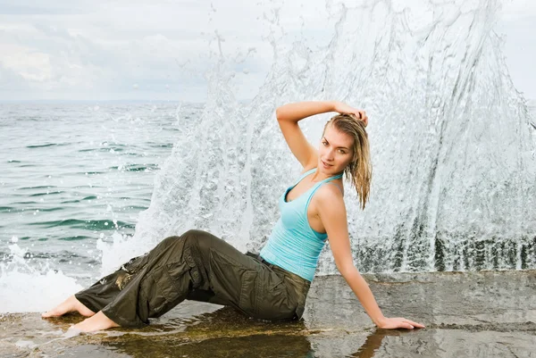 Ragazza bagnata seduta vicino all'oceano. Muro d'acqua dietro di lei — Foto Stock
