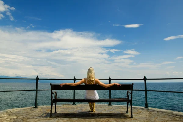 女人坐在一张长凳上和在海上寻找 — 图库照片