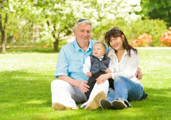Счастливая семья, сидящая на лугу в парке — стоковое фото
