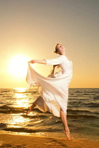 美しい若い女性は夕暮れ時のビーチにジャンプ — ストック写真