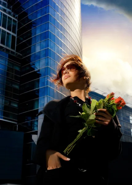 Mooie jonge brunette met rode rozen. modern gebouw achter — Stockfoto