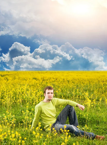 Ontspannen jonge man zit in een bloem veld — Stockfoto