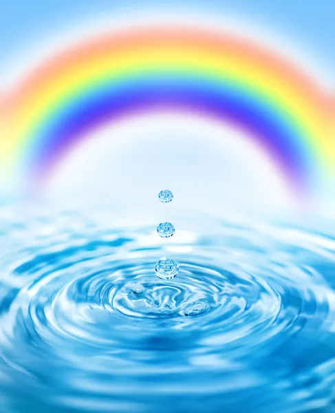 Raindrops falling into water and colorful rainbow behind it — Stock Photo, Image