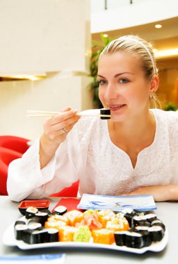 Beautiful girl eating sushi in a restaurant clipart