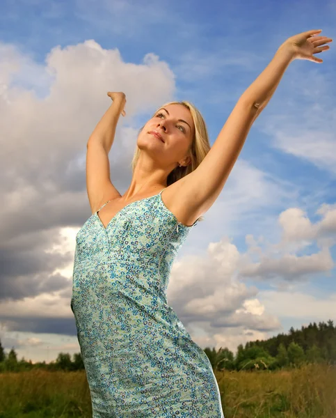 Mooie jonge vrouw over blauwe bewolkte hemel — Stockfoto