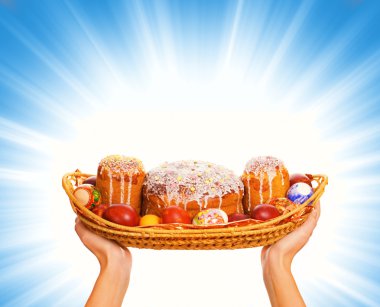 Hands holding woven basket full with easter eggs and easter cakes clipart