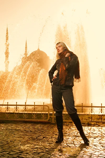 Vacker blond flicka står nära fontänen vid solnedgång — Stockfoto