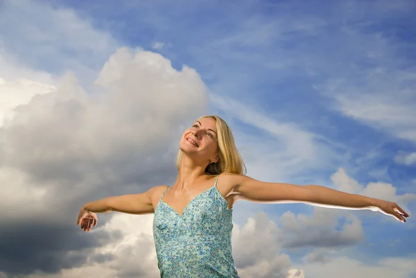 Hermosa chica rubia con los brazos abiertos sobre el cielo nublado azul — Foto de Stock