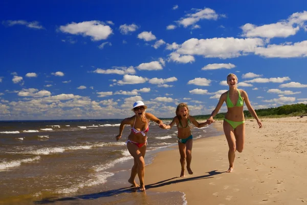 母と二人の娘 水の近くのビーチで実行されています — ストック写真
