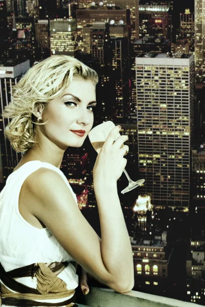 Beautiful blond girl drinks champagne on a skyscraper in megapol — Stock Photo, Image