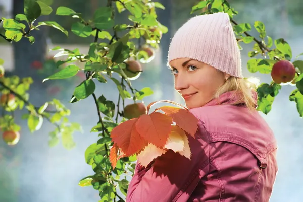 Vacker flicka med höstlöv nära äppelträd och blå f — Stockfoto