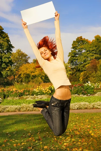 秋の背景に白の掲示板付きジャンプ美しい赤毛の女の子 — ストック写真