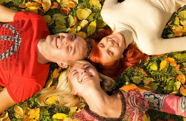 Três amigos deitados em folhas de outono — Fotografia de Stock